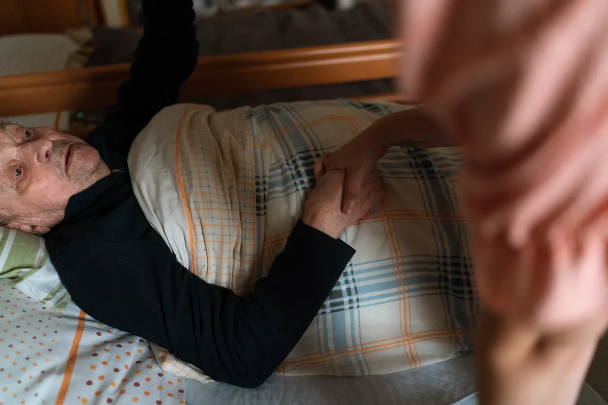 Care worker holding the hand of an older adult resting in bed