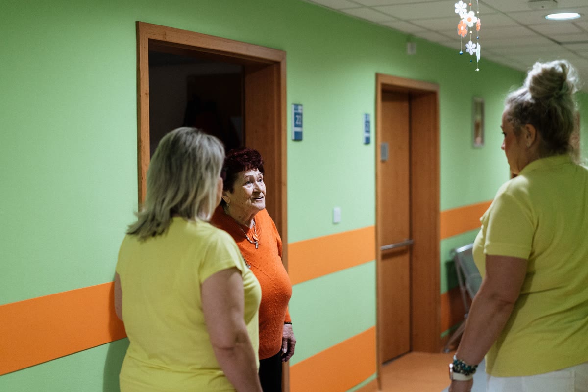 Older woman speaking with two care workers in a residential hallway