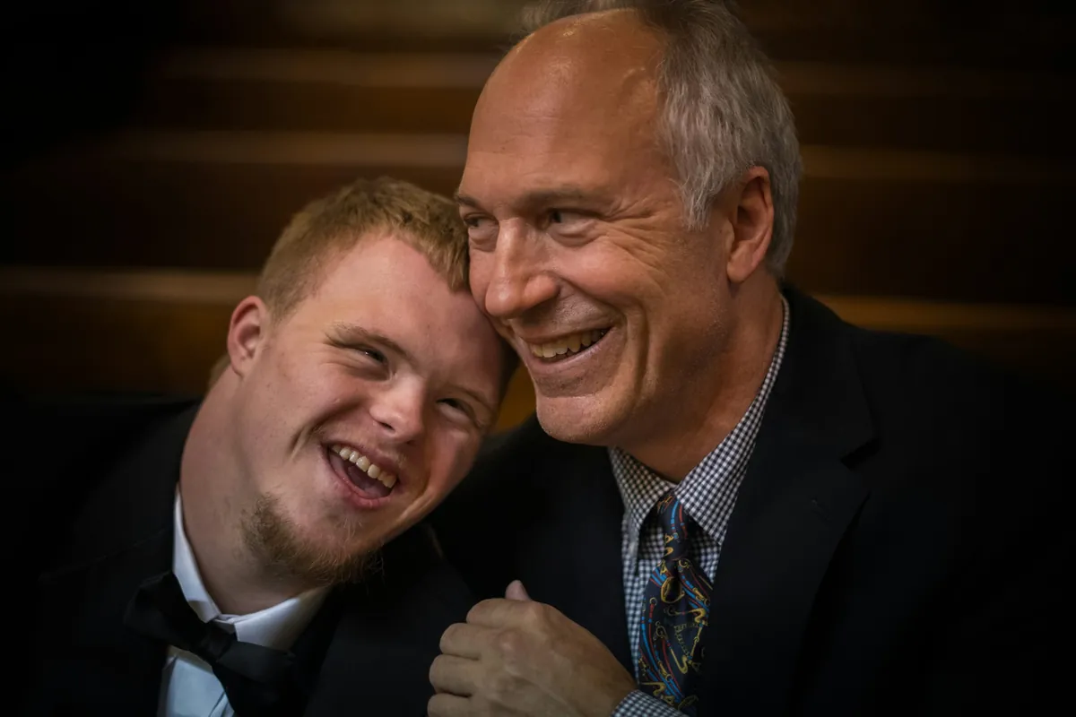 Adult man with Down syndrome smiling beside an older family member